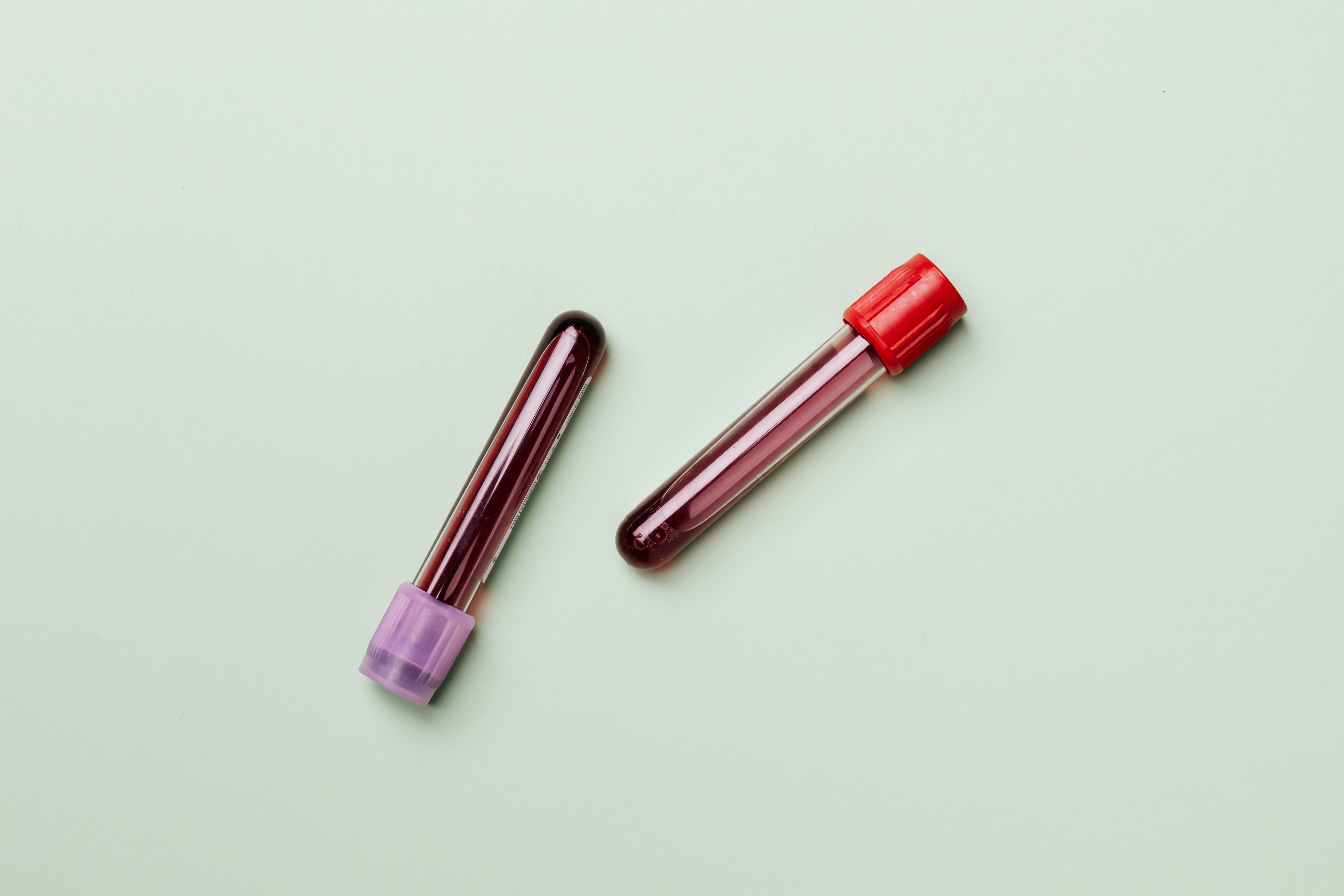 Zwei Röhrchen mit Blut auf Pastellfarbenem Hintergrund Zwei Röhrchen mit Blut auf Pastellfarbenem Hintergrund