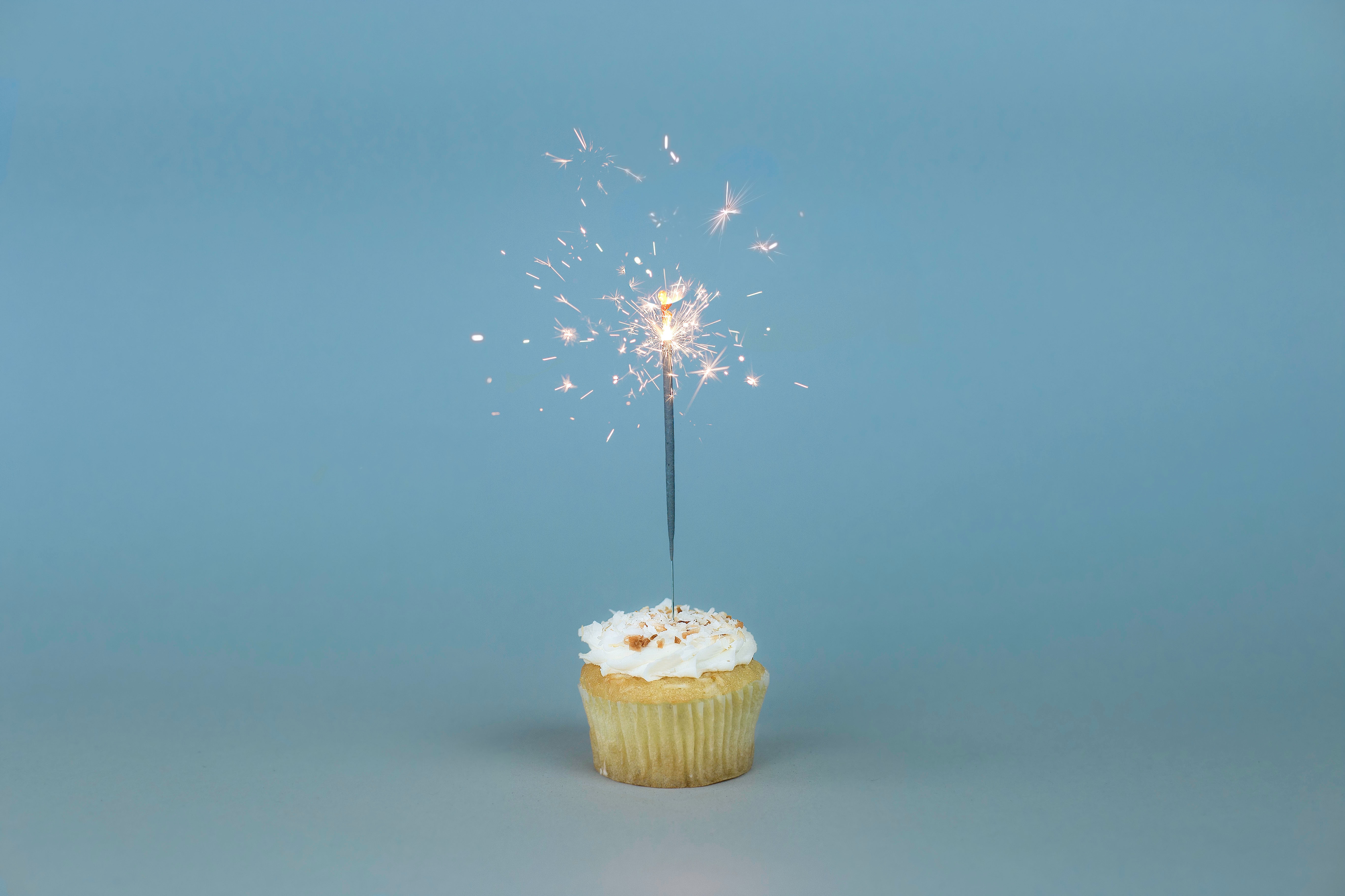Foto von einem Muffin mit einer brennenden Wunderkerze vor hellblauem Hintegrund