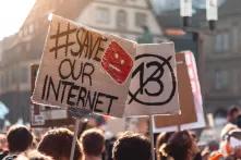 someone holding a poster on a demonstration with the words "#save our internet" written on it