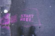 the words "start here" written on asphalt in pink color