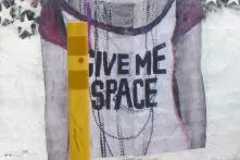 Streetart mit dem Text "Give me space" auf dem weissen T-Shirt einer Person. 