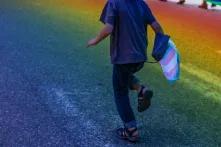 Junge Person laeuft mit Transflagge auf Asphalt, der in Regenbogenfarben scheint