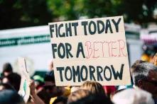 Im Bild ist eine Demonstration zu sehen, im Fokus steht ein Plakat auf dem steht: FIGHT TODAY FOR A BETTER TOMORROW