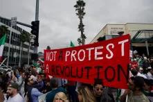 Auf em Foto ist eine Demonstration zu sehen, mehrere iranische Flaggen werden hochgehalten. In der Mitte ist ein rotes Banner, auf dem Steht - Not a protest, a revolution. Im linken oberen Bildrand ist ein Straßenschild abgebildet, auf dem steht: Do not block intersection. 