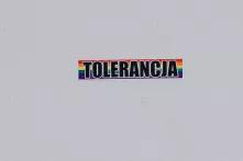 Auf einem Sticker mit Regenbogen Hintergrund steht auf polnisch das Wort "Toleranz". Der Sticker klebt auf einer weißen Wand.