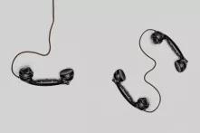 Drei schwarze Telefonhörer mit Kabel vor grauem Hintergrund