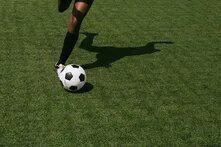 Im Anschnitt wird ein Bein dargestellt, welches einen Fußball führt und kurz davor ist ihn wegzuschießen.