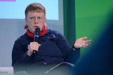 Podium Person auf Podium spricht in Mikro und gestikuliert ernst und sachlich