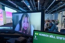 Pin Lean Lau Person live per Video zugeschalten redet, Podium im Hintergrund