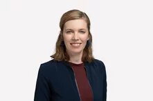 Person mit schulterlangem blonden Haar und der Kamera zugewandt lächelnd vor hellem Hintergrund.