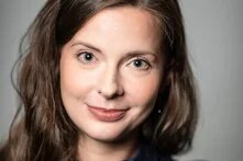 Weiblich gelesene normschöne Person blickt freundlich in die Kamera. Sie hat lange braune Haare, graugrüne Augen, ist weiß und etwa mitte Dreißig. Ich Kopf ist leicht geneigt und sie wirkt einladend bis auffordernd fröhlich.