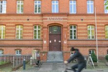 Ein Fahrradfahrer fährt an einem rot geklinkertem Radhaus vorbei. Das bild wirkt statisch und trotz Person, verlassen.
