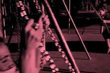 Wir sind mitten zwischen den Schaukeln eines Spielplatzes: ein kleines Kind schaukelt und guckt lachend eine erwachsene weibliche Person an die ebenfalls forne im Bildrand schaukelt. Über allem liegt ein altrosa Film.