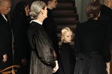 Ein blondes Mädchen steht zwischen weiteren Personen und blicktin die Kamera.