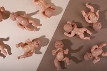 Babypuppen aus Plastik liegen entlange einer Trennline von hell zu dunkel Braun. 