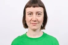 Person frontal fotografiert mit grünem Oberteil und hellbraunen kinnlangen Haaren