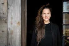 Theresa Leisgang steht in schwarzem Oberteil undlangem brauen Pferdeschwanz vor einem Gebäudeeingang