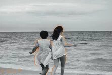 Photo: Two people run toward the sea on the beach. They are shown in black and white with orange outlines. "RESIST" is written in the bottom left.