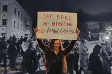 Photo: A protest scene at night with many people marching. A woman in the foreground, highlighted in color, holds a sign in Macedonian. The word "RESIST" is written in the bottom left corner.