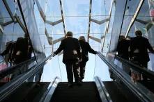 Mann udn Frau in Businesskleidung auf einer Rolltreppe, auf dem Weg nach oben.