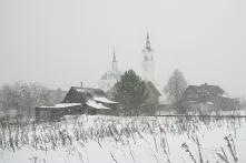 Häuser, Scheunen und Kirche eines russischen Dorfes im Schneeschauer