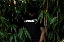 Eine Person steht vor Pflanzen. Auf ihrem T-Shirt steht: Equality