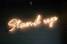 Leuchtzeichen mit der Schrift "Stand up" frontal fotografiert vor dunklem Hintergrund