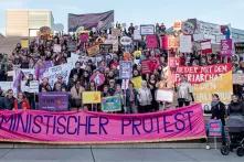 Eine Gruppe von circa 200 Demonstrierenden steht auf einer Treppe im Freien für ein Gruppenfoto. Sie tragen Protestschilder und Plakate. Im Fordergrund tragen Leute ein Banner mit der Aufschrift: Feministischer Protest