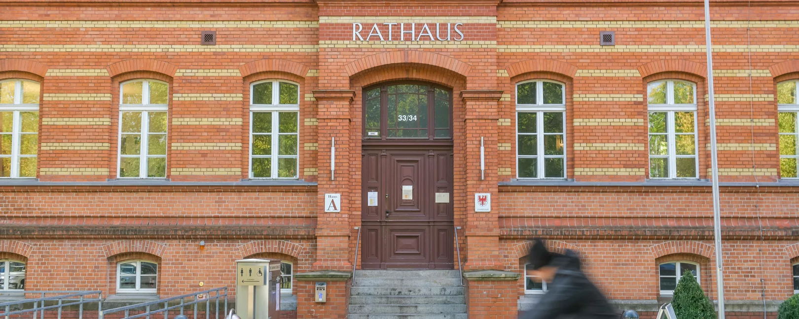 Ein Fahrradfahrer fährt an einem rot geklinkertem Radhaus vorbei. Das bild wirkt statisch und trotz Person, verlassen.