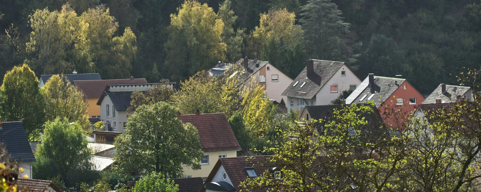 Am Hang eines Berges liegen moderne Einfamilienhäuser. Eines hat einen geschmacklosen Erker. Das Licht ist sanft und angenehm.
