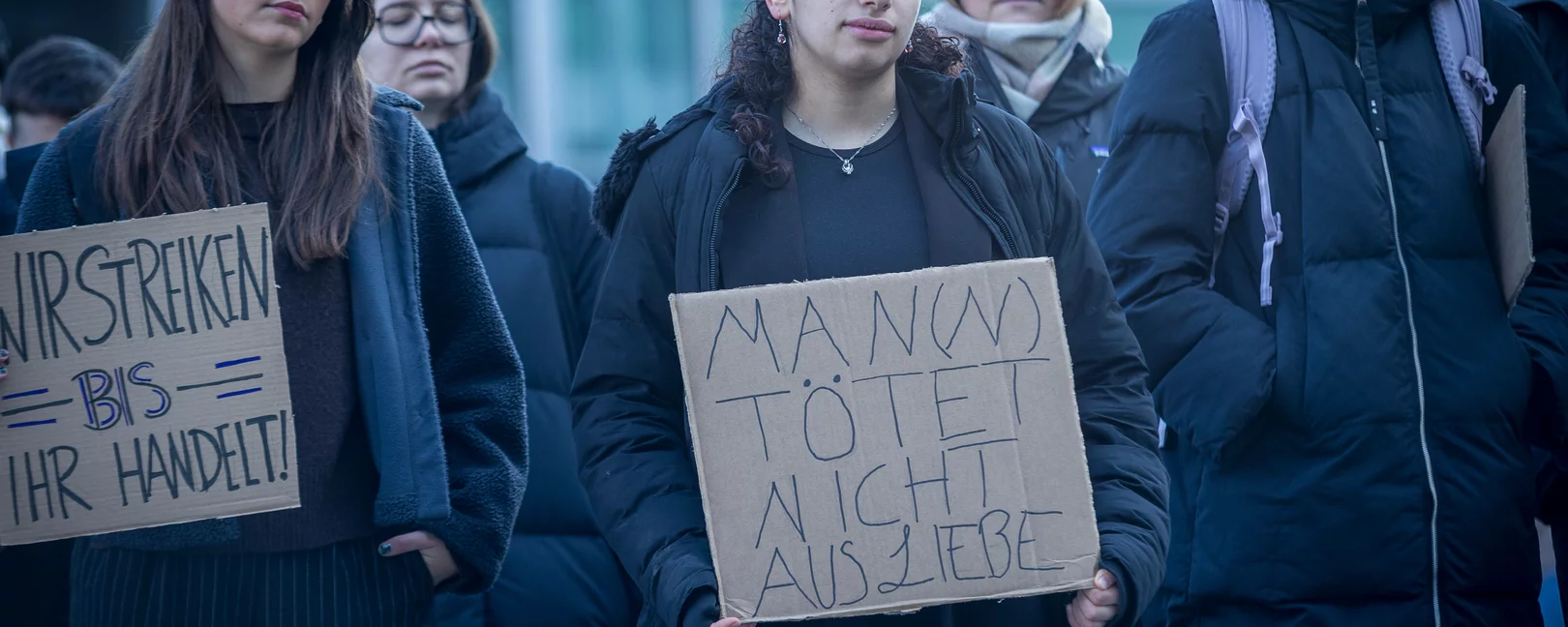 Eine Gruppe von Frauen protestiert in Köln gegen Femizide. Zu sehen ist eine Fraue mit einem Protestschild mit der Aufschrift: Man(n) tötet nicht aus Liebe
