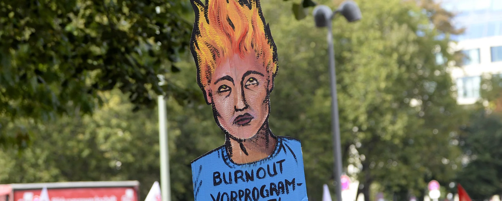 Ein Plakat auf einer Demo steht im Mittelpunkt: die Haare einer erschöpften Menschlichen Figure 