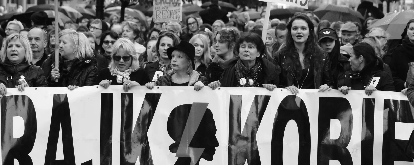Ein schwarz weiß Foto einer feministischen Demonstration in Polen zu Schwangerschaftsabbrüchen. Sie halten ein Transparent auf dem steht 