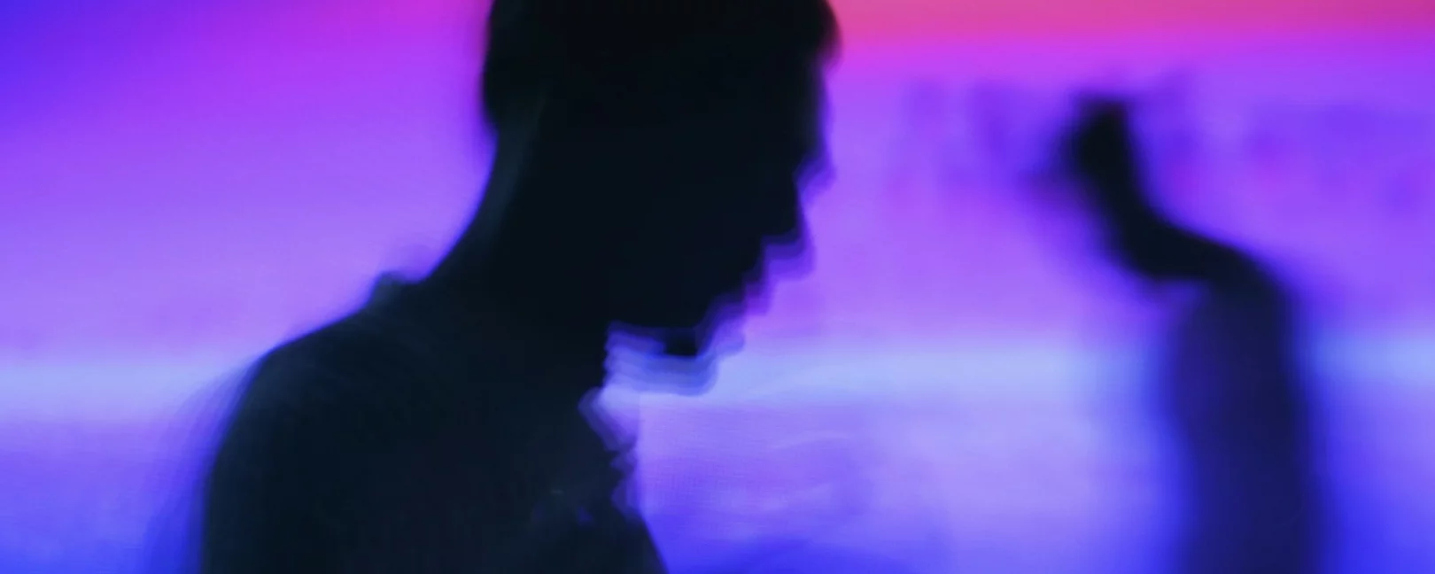 Zwei Silhouetten vor buntem Hintergrund/Licht.