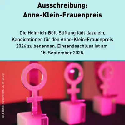 Drei Pokale des Anne-Klein-Frauenpreises, die aussehen wie das Weiblichkeitssymbol auf einem kleinen Sockel, werden rosa angeleuchtet. 