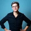 Susanne Weise Vor blauem Grund steht, die Hände in die Hüften gestützt, schwarz gekleidet eine schlanke Person in ihren frühen 40ern. Die Haare sind kurz, der Blick durch eine Brille lächelt Betrachtende direkt an.