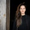 Theresa Leisgang steht in schwarzem Oberteil undlangem brauen Pferdeschwanz vor einem Gebäudeeingang