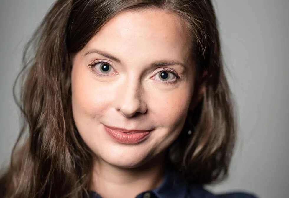 Weiblich gelesene normschöne Person blickt freundlich in die Kamera. Sie hat lange braune Haare, graugrüne Augen, ist weiß und etwa mitte Dreißig. Ich Kopf ist leicht geneigt und sie wirkt einladend bis auffordernd fröhlich.