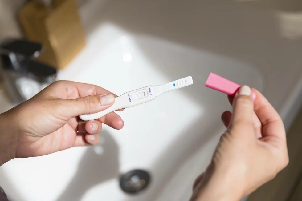 Safe Abortion Day Ein Schwangerschaftstest ist positiv ausgefallen. Zwei weisse weibliche Hände halten ihn über einem sonnenbeschienen Waschbecken. Es wirkt wie eine Point-of-View-Aufnahme.
