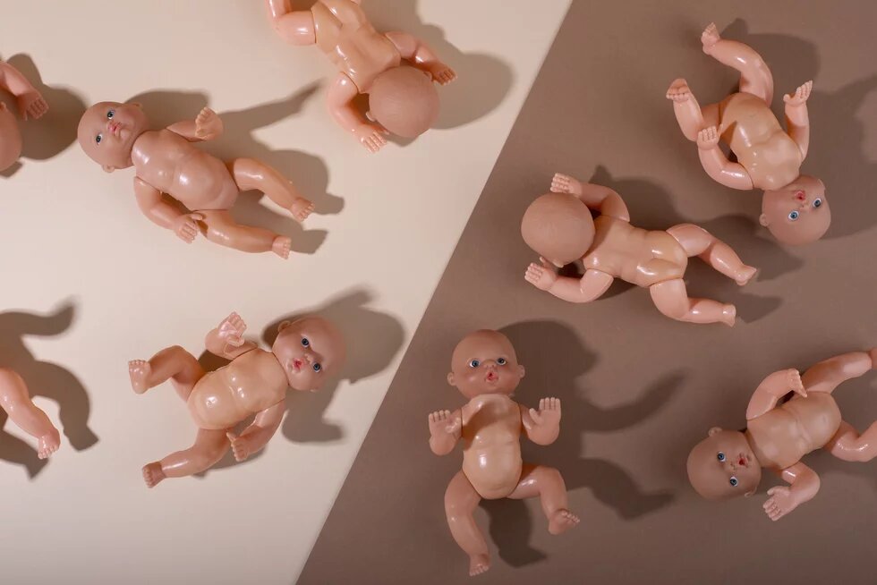 Babypuppen aus Plastik liegen entlange einer Trennline von hell zu dunkel Braun. 