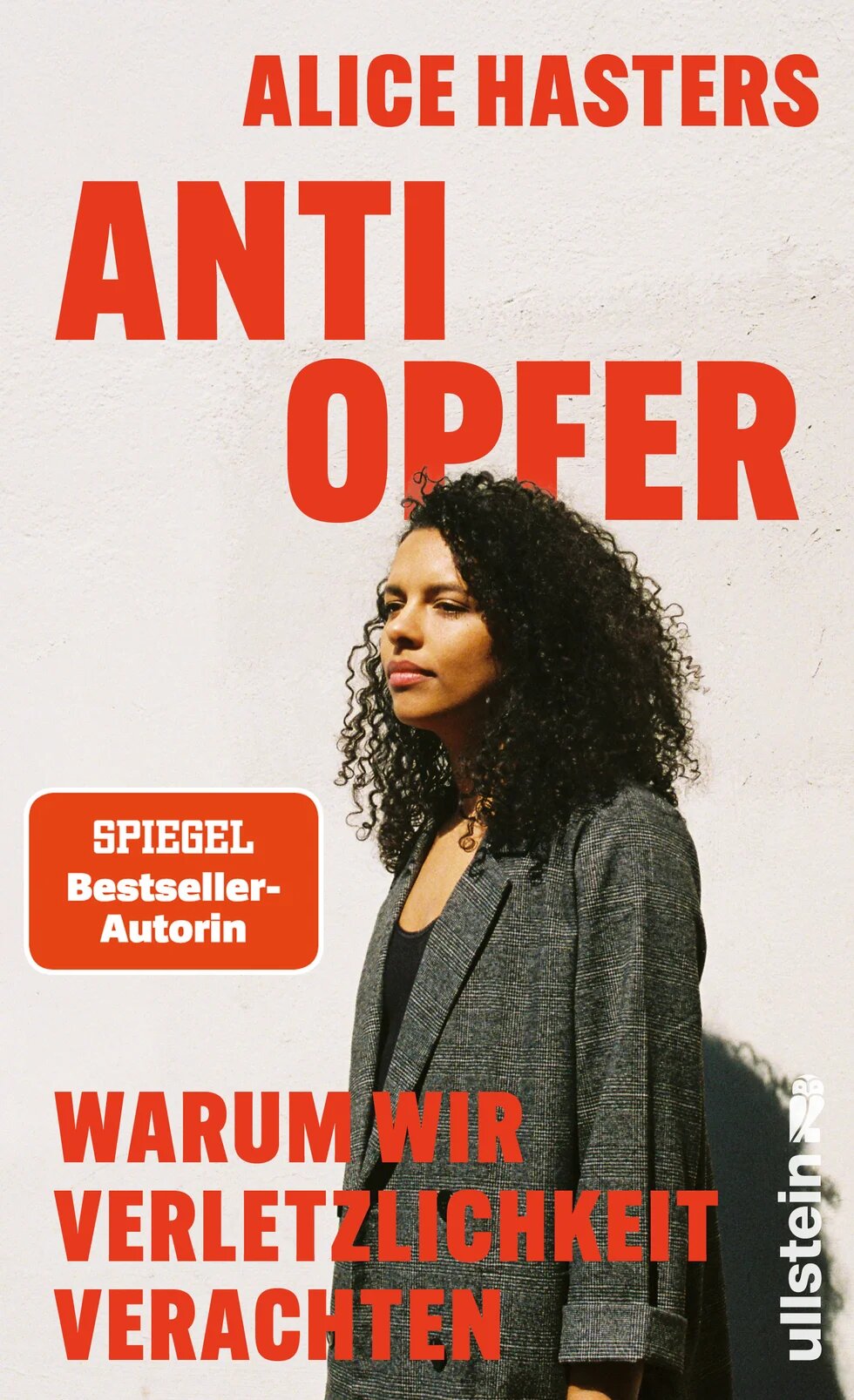 Buchcover mit dem Titel "Anti Opfer" von Alice Hasters mit dem Untertitel "Warum wir Verletzlichkeit verachten" in roter Schrift. Alice Hasters seitlich stehend in einem grauen Blazer abgebildet.