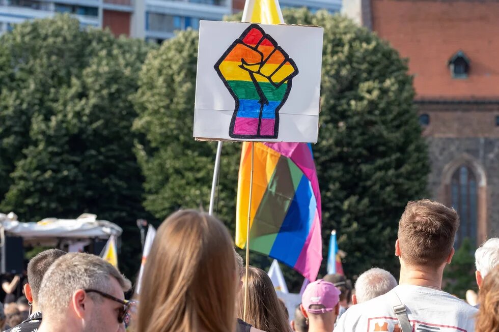Ein Demoschild, das eine Faust in Regenbogenfarben abbildet, in einer Menschenmenge