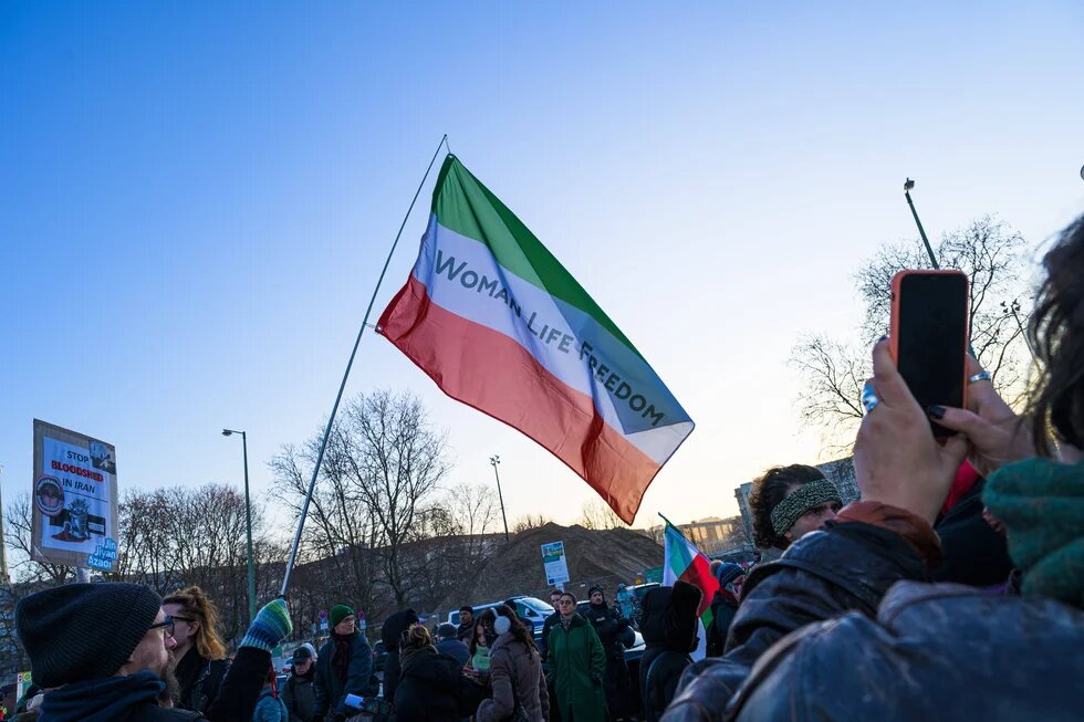 Eine grün-weiß-rote Flagge des Irans mit dem Schriftzug "Women Life Freedom"