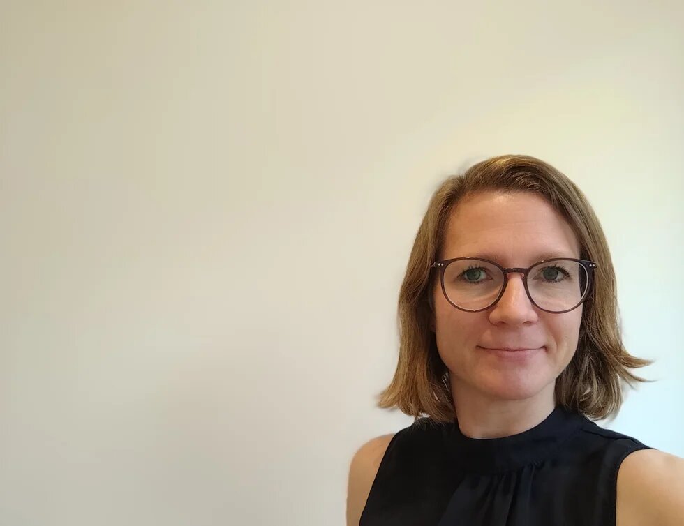 Person mit blonden mittellangen Haaren und einer schwarzen Brille blickt freundlich in die Kamera.