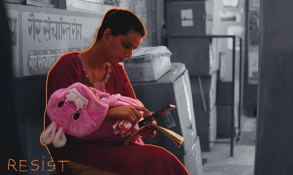 Photo: A woman in traditional clothing sits on a bench, holding a baby wrapped in a pink blanket. She looks at her phone while holding an open book. The word "RESIST" is written in the image.