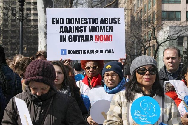Weltweit eines der drängendsten Probleme: die Gewalt gegen Frauen, häusliche, sexualisierte, Kriegsgewalt. Teilnehmerinnen der Demo zum 08.03.2015 in new York - Plakat mit Aufschrift :"end domestic abuse against women in guyana now"