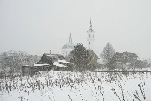The Church of Archangel Michael in Podzhigorodovo Häuser, Scheunen und Kirche eines russischen Dorfes im Schneeschauer