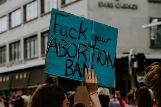 someone holding a poster on a demonstration with the words "fuck your abortion ban" written on it