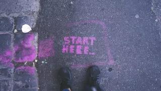 the words "start here" written on asphalt in pink color