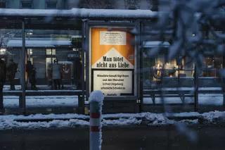 Plakat mit Aufschrift "Man tötet nicht aus Liebe - Männliche Gewalt fügt Ihnen und den Menschen in Ihrer Umgebung erhebliche Schäden zu" im Stil der Warnungen auf Zigarettenschachteln an einer verschneiten Bushaltestelle.
